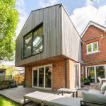 Picture of a red brick and flint house that has a mid tone timber clad extension that has a cantilever.