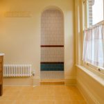 A yellow bathroom with a arched reveal showing the shower alcove that has white tiles with bands of red and blue tiles